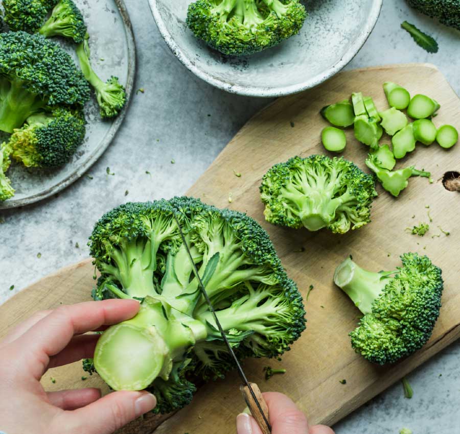 Scheinfasten mit frischen Lebensmitteln Hand schneidet Brokkoli, ein Symbol für die gemüsebasierten und gesunden Rezepte während des Scheinfastens.