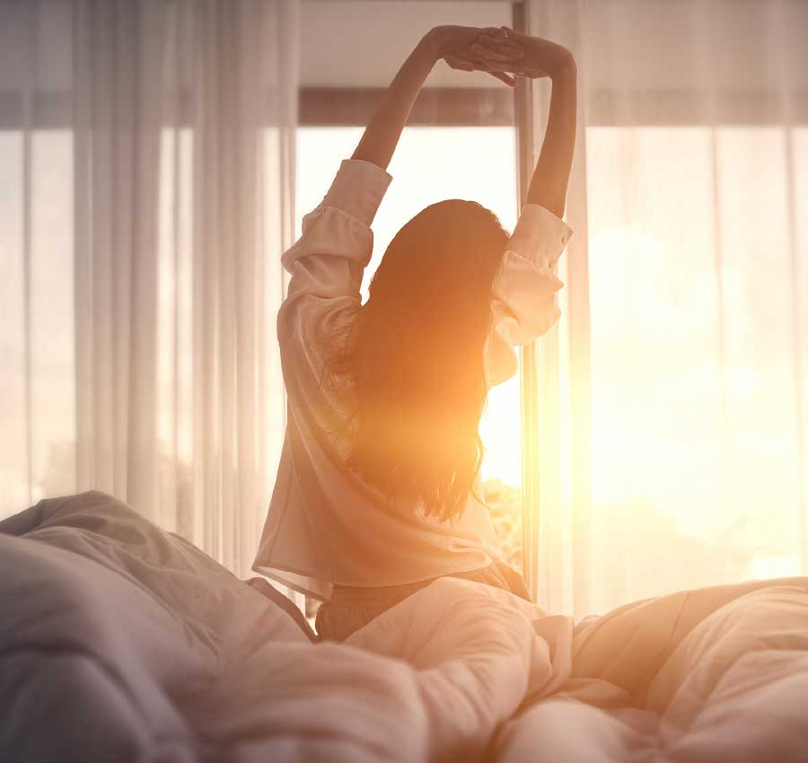 Gesunder Schlaf für körperliche und geistige Gesundheit Frau streckt sich im Bett bei Sonnenaufgang – Erholsamer Schlaf für Vitalität und Gesundheit